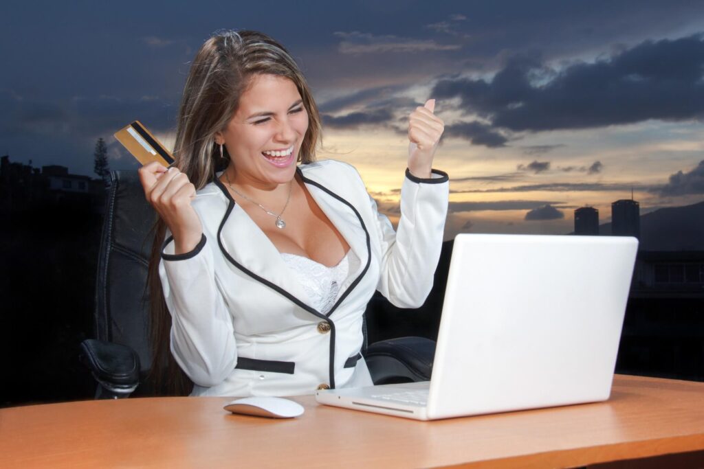 a woman swinging her credit card in front of a laptop, representation of the result of good marketing